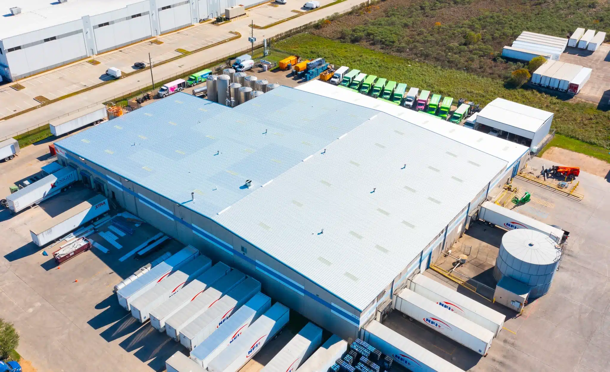 ds services1 Aerial view of a large commercial roofing facility with loading docks, trailers, and rooftop drainage features.