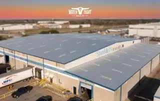 Aerial view of a large industrial building with a single ply membrane commercial roof at sunset, illustrating WaterTight Roofing’s guide to roof components.