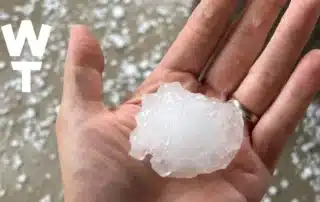 Large hailstone held in a hand illustrating how extreme weather and temperature swings can affect commercial roofs