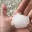 Large hailstone held in a hand illustrating how extreme weather and temperature swings can affect commercial roofs