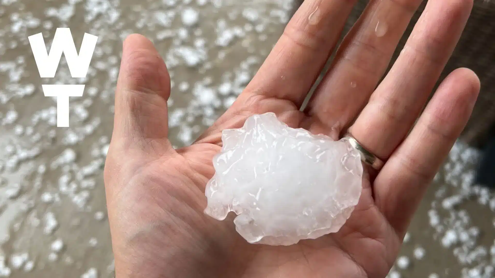 Large hailstone held in a hand illustrating how extreme weather and temperature swings can affect commercial roofs